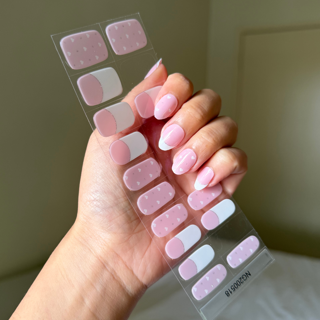 Hand holding a sheet of gellae pink nail stickers with love hearts and white french tipon a neutral background