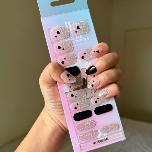 Hand holding a package of gellae nail stickers with black and silver hearts a person wearing matching nail designs.