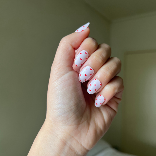 Hand with pink nail gellae featuring red heart designs against a neutral background