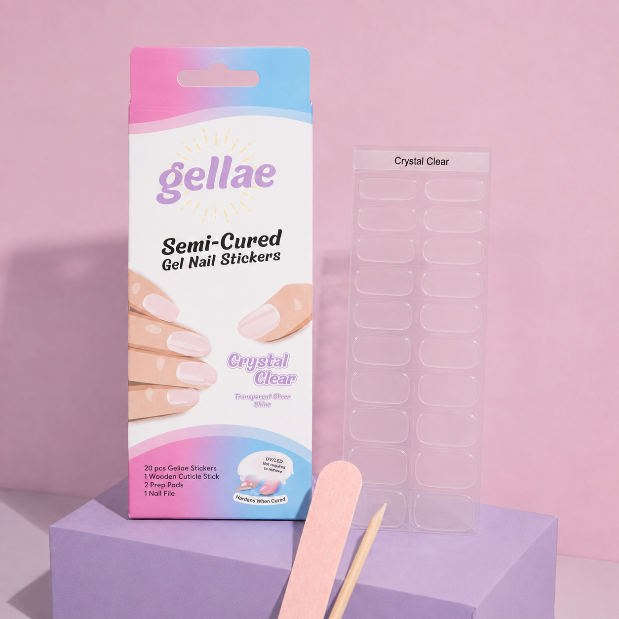Gellae Semi-Cured Gel Nail Stickers in 'Crystal Clear' packaging, shown next to a sheet of clear nail stickers and wooden nail tools on a pink and purple block setup.