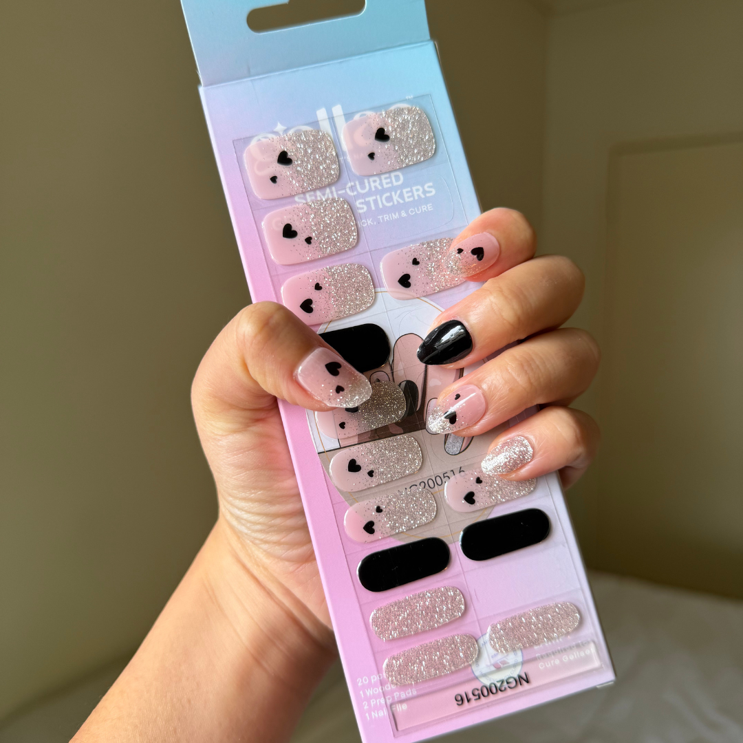 Hand holding a package of gellae nail stickers with black and silver hearts a person wearing matching nail designs.